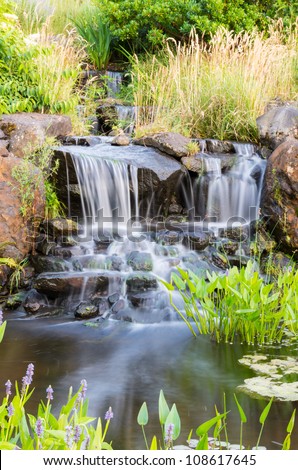 A flowing waterfall with grass and flowers in the park