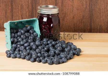 Blueberries spilling onto a wooden table with a jar of blueberry jam or jelly