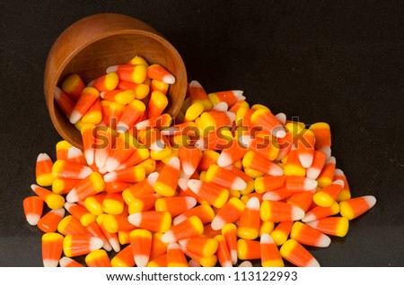 Candy corn spilling from a wooden bowl on black table