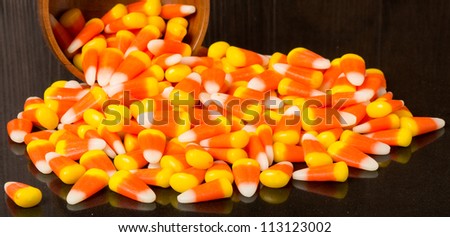 Candy corn spilling from wooden bowl onto black table