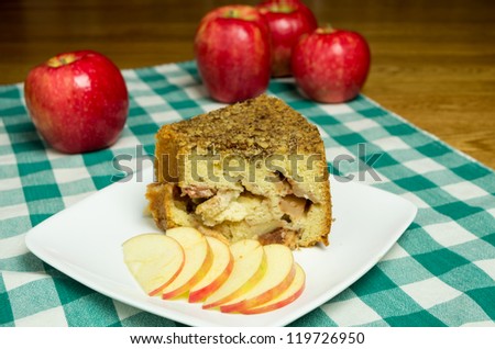 Slice of apple cake on white plate with red apple