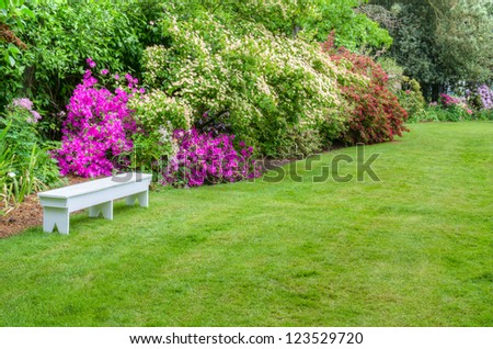 A garden scene with blooming azaleas and a white bench