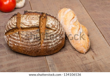 A loaf of fresh rye bread on a table with french baguette