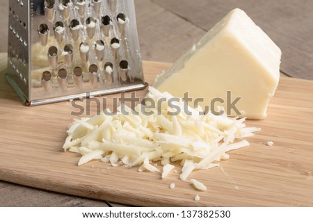 Fresh Parmesan cheese with a metal grater on a cutting board