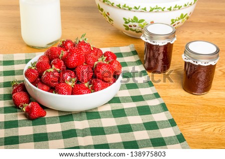 Bowl of fresh strawberries with milk and jars of jam or jelly