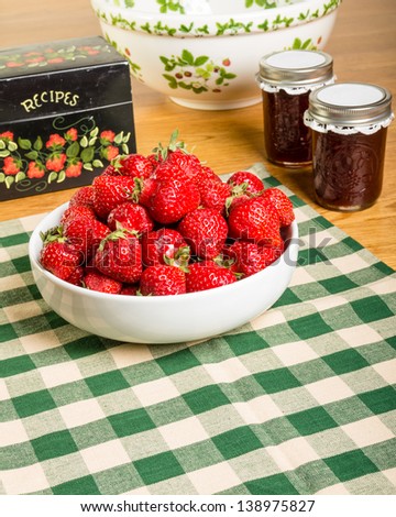 Bowl of fresh strawberries with jars of jam or jelly