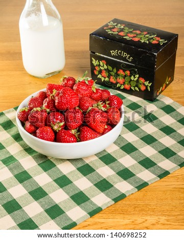 A bowl of fresh strawberries with a recipe box and a milk bottle