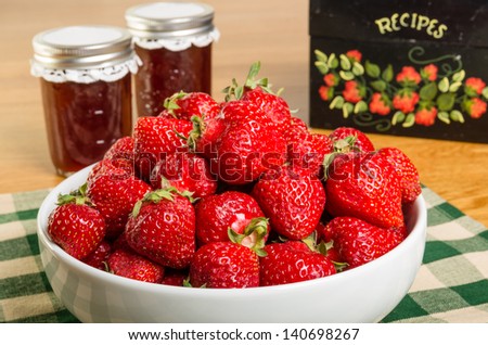 Bowl of fresh strawberries with jars of jam or jelly