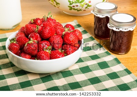 Bowl of fresh strawberries with milk and jars of jam or jelly