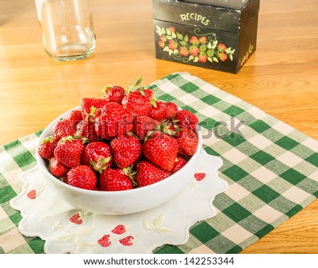A bowl of fresh strawberries with a recipe box and a milk bottle