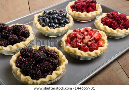 Six homemade fresh fruit pies on a tray made with strawberries raspberries blueberries blackberries