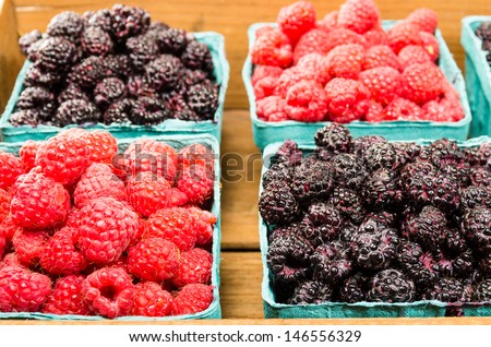 A wooden box with baskets of red raspberries and black raspberries