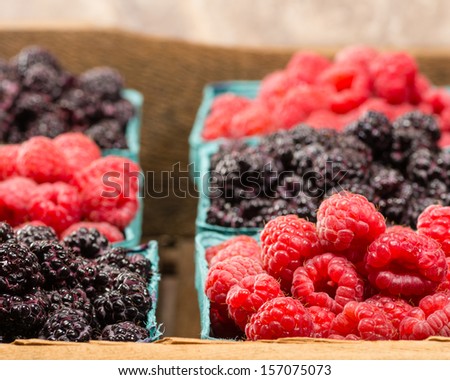 A wooden box with baskets of red raspberries and black raspberries