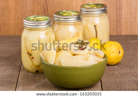 A bowl of fresh canned spiced pears with jars of pears