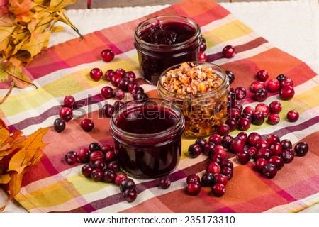 Jars of cranberry sauce with cranberries and fall leaves on a table