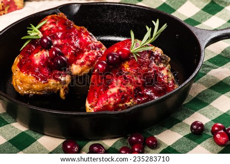 Two cranberry glazed chicken breasts in a cast iron skillet with berries