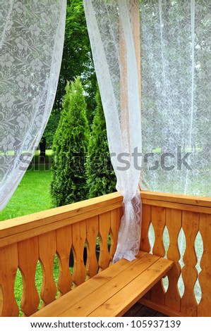 Wooden porch with lace curtains and garden view