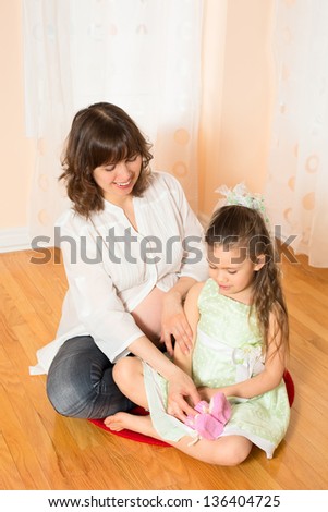 Pregnant Woman Showing Her Daughter Hand-Knitted Baby Clothes