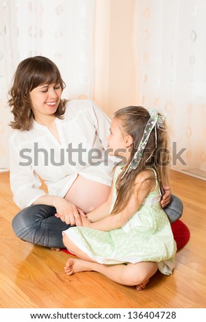 Pregnant Woman Talking Some Happy Matters with Her Daughter Sitting on the Floor in the Living Room