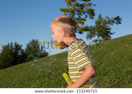 A school-aged boy makes soap bubbles in summer park