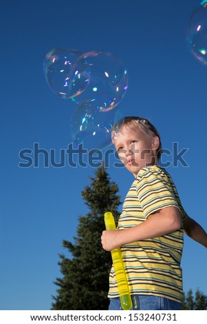 A school-aged boy makes soap bubbles in summer park