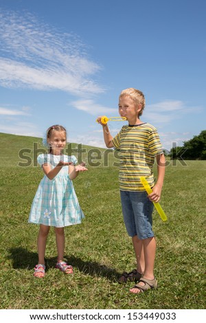 A boy makes soap bubbles and a girl tries to catch them in a summer park