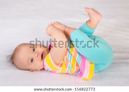Little baby girl lying on her back and reaching to her foot while looking at the camera