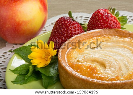 Apple tart with strawberries, mint, a flower of calendula on a plate, with an apple on a background