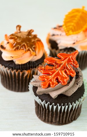 Fall concept: three delicious cupcakes with plastic top leaves on top of them, against light grey background
