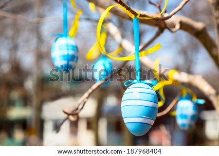 Colored hand-crafted easter eggs hanging from a tree in a park in early spring
