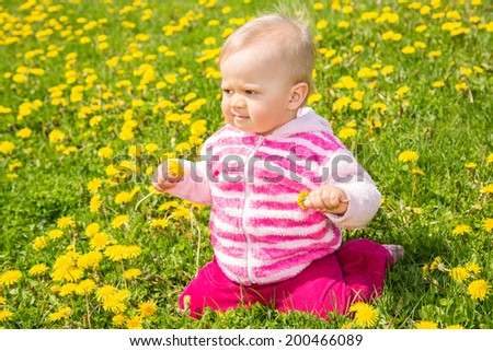 Baby girl sitting in a dandelion field, holding two dandelions in her hands