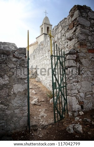 Open gate in old stone wall with church in background