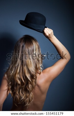 Naked woman standing back holding hat above head