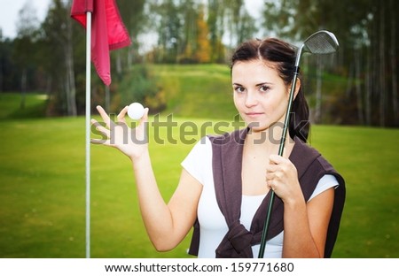 Young woman golf player on green with ball and club near cup flag