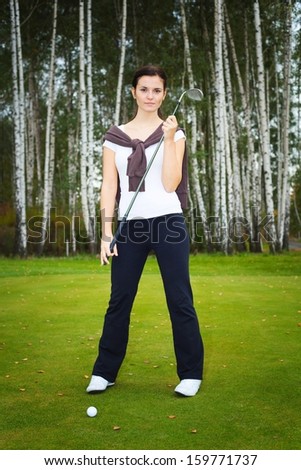 Young woman golf player posing on green with club and ball