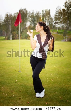 Young woman golf player on green kissing ball