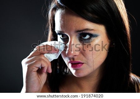 Hurt woman crying, face with smeared make up on dark background