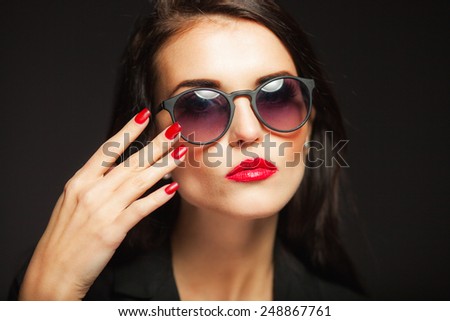 Beautiful glamour woman with fashion sunglasses, red lips and nails on dark background