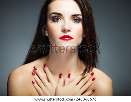 Natural woman face with red nails and lips on dark background