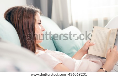 Young woman lying on couch and reading a book at home, casual style indoor shoot