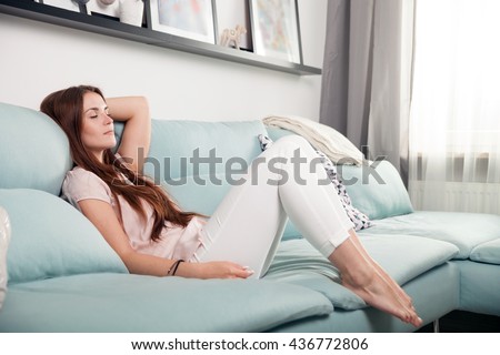 Happy young woman lying on couch and relaxing at home, casual style indoor shoot