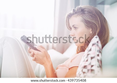 Young woman sitting on couch at home and watching TV, casual style indoor shoot