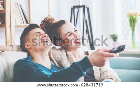 Young loving couple on sofa at home watching tv and laughing
