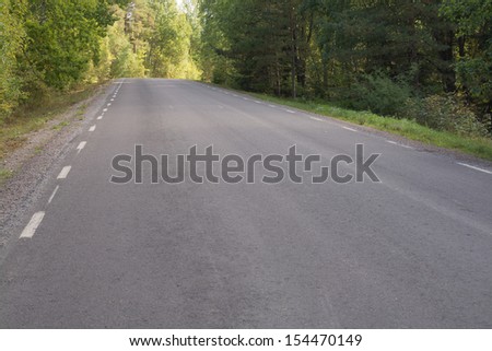 Empty asphalted country road approaching a hill, through a forest in Sormland, Sweden.