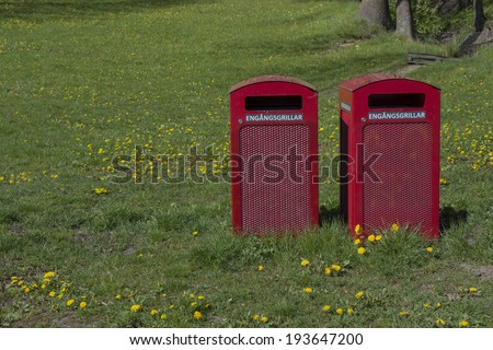 Two red garbage bins with text 'engangsgrillar' for disposable barbecue items in a park, Stockholm, Sweden in May.