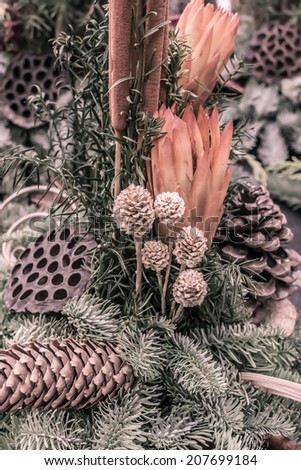 Decorative autumnal flower arrangement with cones and spruce twigs in oranges and green, vertical image.