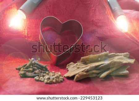 Christmas background. Heart baking tin and raw spices - cinnamon, cardamom and cloves - on red silk fabric with two christmas lights.