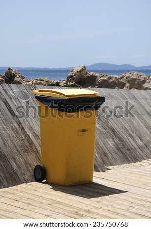 CALA ESTANCIA, MAJORCA, SPAIN - JULY 21 2012: Large yellow trash bin keeps the garbage away from the wooden jetty on July 21 2012 in Cala Estancia, Mallorca, Balearic islands, Spain.