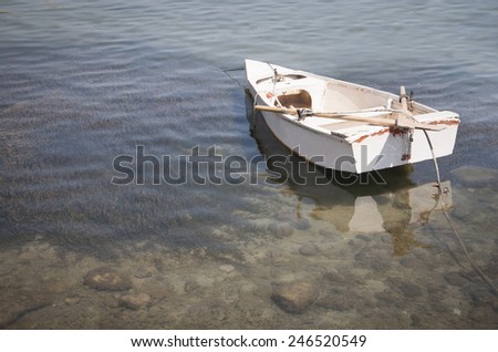 Old white row boat moored on peaceful shallow and transparent water.