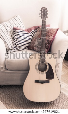 STOCKHOLM, SWEDEN - FEBRUARY 17, 2014: Interior detail of Fender acoustic guitar leaning against armchair with pillows on February 17, 2014 in Stockholm, Sweden.